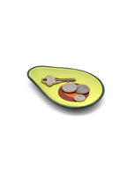 Avocado-shaped trinket tray holding coins and a key on a white background.