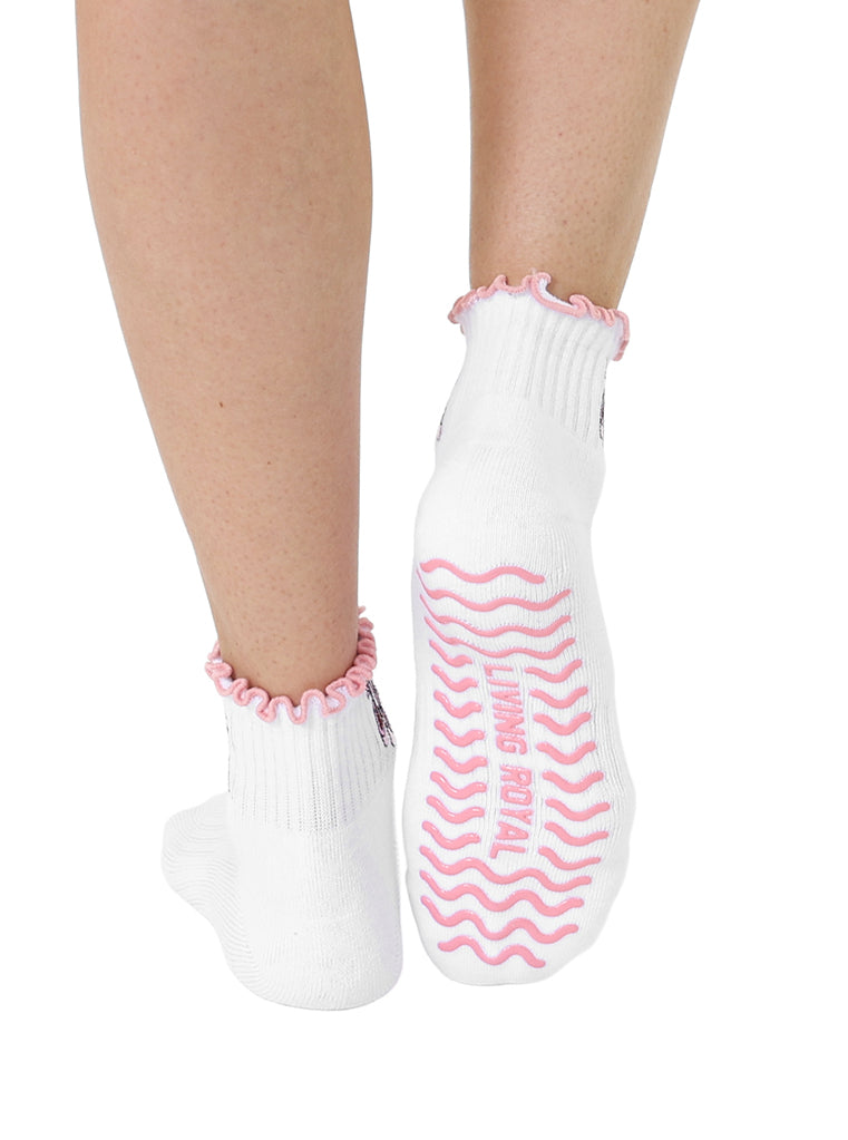 White socks with pink lining, equipped with stay-put grips to prevent slipping, featuring a small ballet-themed print, shown worn on a white background.