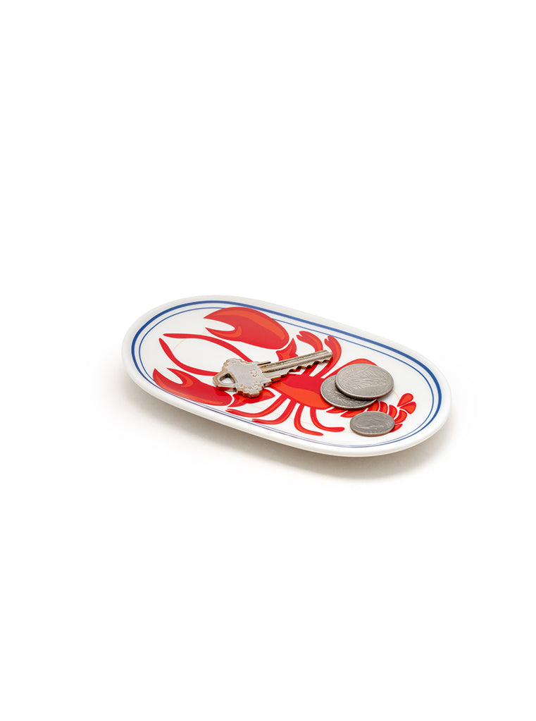 White oval-shaped trinket tray with lobster  print holding coins and a key on a white background.