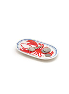 White oval-shaped trinket tray with lobster  print holding coins and a key on a white background.