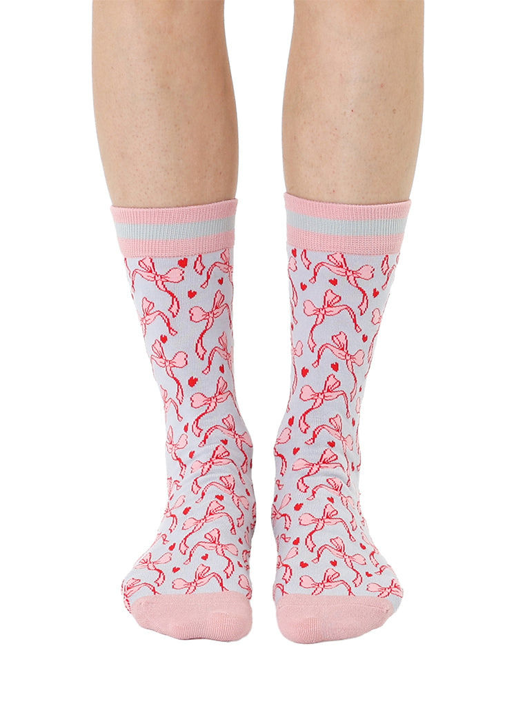 Pink and grey women’s bamboo crew socks featuring a delicate bow pattern print, shown worn on a person against a white background.