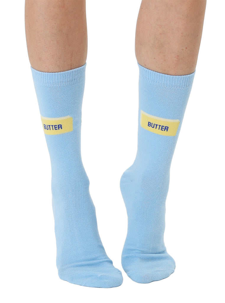 Light blue socks with yellow 'BUTTER' text worn by a person on a white background