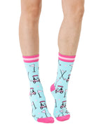 Light blue women’s bamboo crew socks with pink-striped cuffs, featuring a playful golf-themed print, shown worn on a person on a white background.